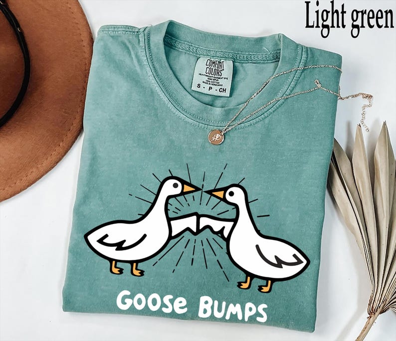 May include: A light green t-shirt featuring a white goose design and the text "Goose Bumps".