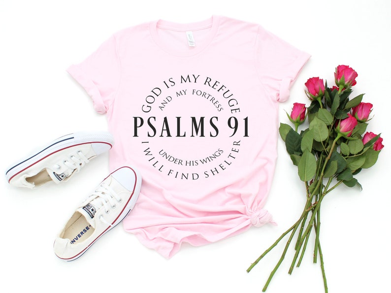 May include: A pink t-shirt with a black circle graphic that says "God is my refuge and my fortress, Psalms 91, Under his wings I will find shelter".