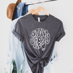 May include: A dark gray t-shirt with a white graphic that says "Stay Groovy, Dude" in a retro font.