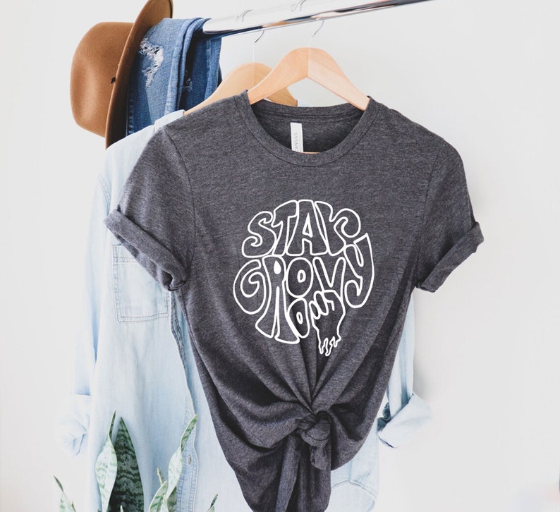May include: A dark gray t-shirt with a white graphic that says "Stay Groovy, Dude" in a retro font.