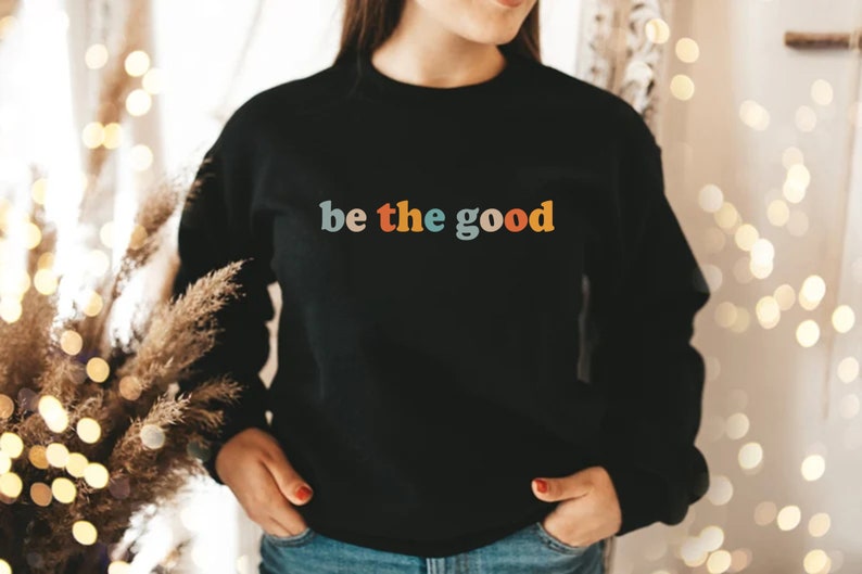 May include: A black sweatshirt with the text "be the good" in colorful letters. The letters are in a retro font style.