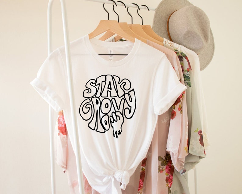 May include: White t-shirt with a black graphic that says "Stay Groovy" in a retro font.