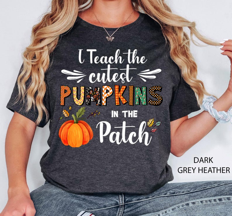 May include: Dark grey heather t-shirt with the text "I Teach the cutest PUMPKINS in the Patch." The word "PUMPKINS" is in orange, green, and black. An orange pumpkin graphic is below the text. The shirt is short-sleeved.