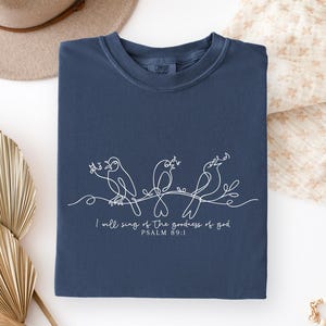 May include: Navy blue sweatshirt featuring a white line drawing of three birds on a branch. The text reads "I will sing of the goodness of God, Psalm 89:1". The sweatshirt is folded neatly.