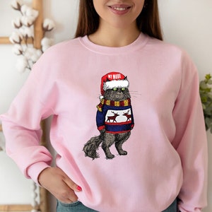 K&ouml;nnte beinhalten: Rosafarbener Pullover mit einem Aufdruck eines Katers, der einen Weihnachtsmann-Hut und einen Rentier-Pullover tr&auml;gt. Der Text "MY MODE" steht auf dem Hut.