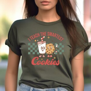 May include: A green t-shirt with a retro-style graphic of a glass of milk and a cookie with the text "I teach the smartest cookies".