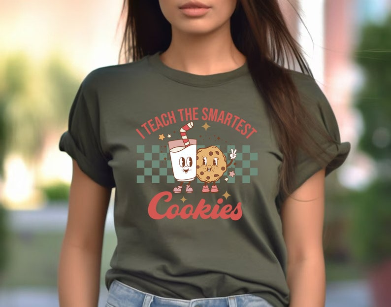 May include: A green t-shirt with a retro-style graphic of a glass of milk and a cookie with the text "I teach the smartest cookies".