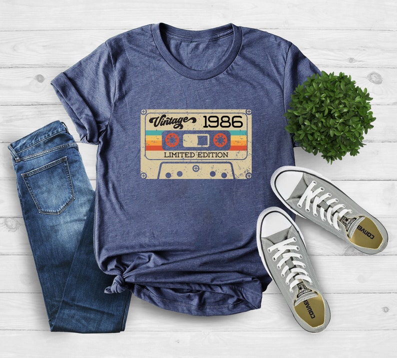 May include: A navy blue t-shirt featuring a vintage cassette tape graphic. The tape has the text "Vintage 1986 Limited Edition" printed on it.