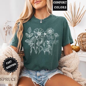 May include: A teal-colored t-shirt with a white floral design. The shirt has short sleeves and a crew neck. The words "COMFORT COLORS" are in a black box in the upper right corner. The words "FAST SHIPPING" are in a black starburst.