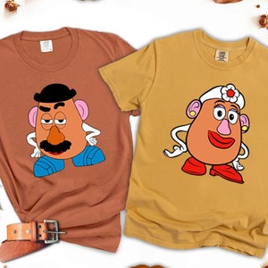 May include: Two brown and yellow t-shirts with a cartoon image of Mr. and Mrs. Potato Head. The shirts are a matching set.
