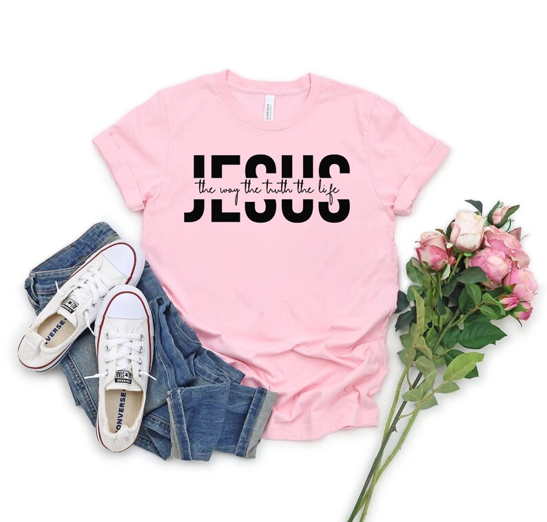 Pu&ograve; includere: Maglietta rosa con testo nero che dice "JESUS the way the truth the life".