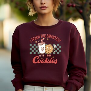 May include: A maroon sweatshirt with a graphic of a glass of milk and a cookie with the text "I teach the smartest cookies".
