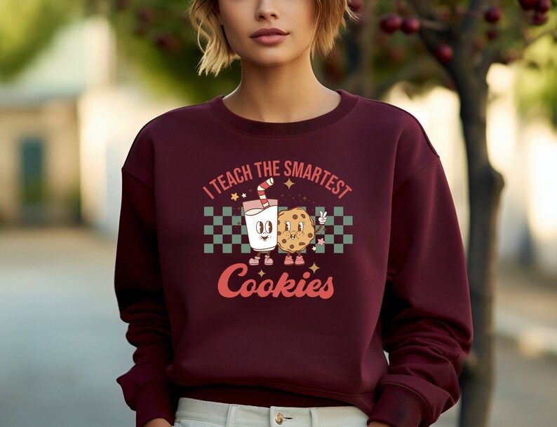 May include: A maroon sweatshirt with a graphic of a glass of milk and a cookie with the text "I teach the smartest cookies".