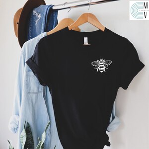 May include: Black t-shirt with a white bee graphic on the front. The bee is stylized with a simple design and has black and white stripes.