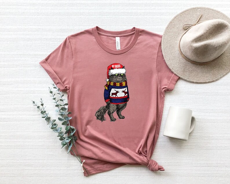 K&ouml;nnte beinhalten: Ein pinkfarbenes T-Shirt mit einem Aufdruck eines Katers, der einen Weihnachtsmann-Hut und einen Weihnachtspullover mit Rentieren tr&auml;gt. Der Text auf dem Hut lautet "My Woof".