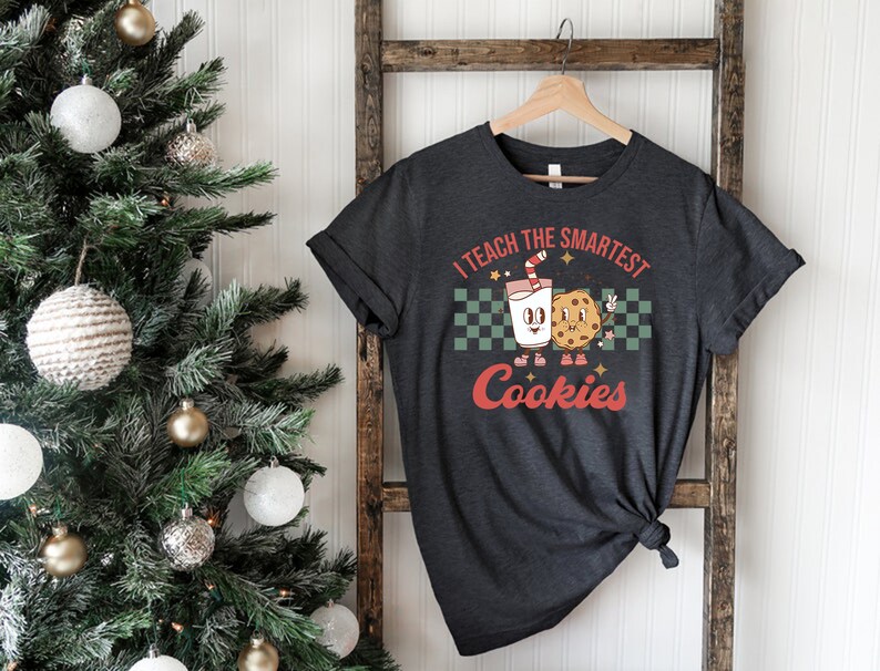 May include: A dark gray t-shirt with a retro design featuring a cartoon glass of milk and a cookie. The text on the shirt reads "I teach the smartest cookies".
