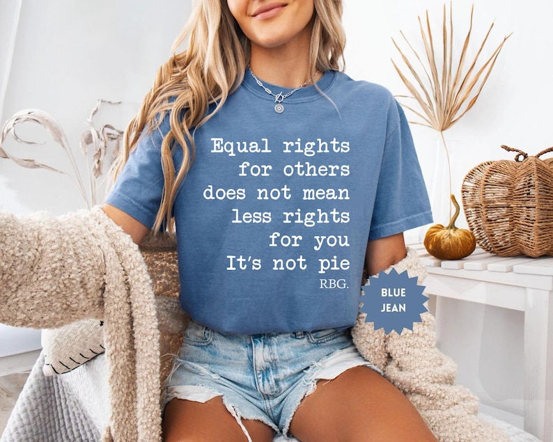 May include: Blue jean colored t-shirt with the quote "Equal rights for others does not mean less rights for you. It's not pie. RBG." The shirt is a short-sleeved, crew neck style.