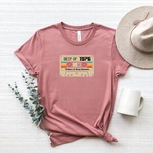 May include: A pink t-shirt featuring a vintage cassette tape graphic that reads "Best of 1976" and "43 Years of Being Awesome".