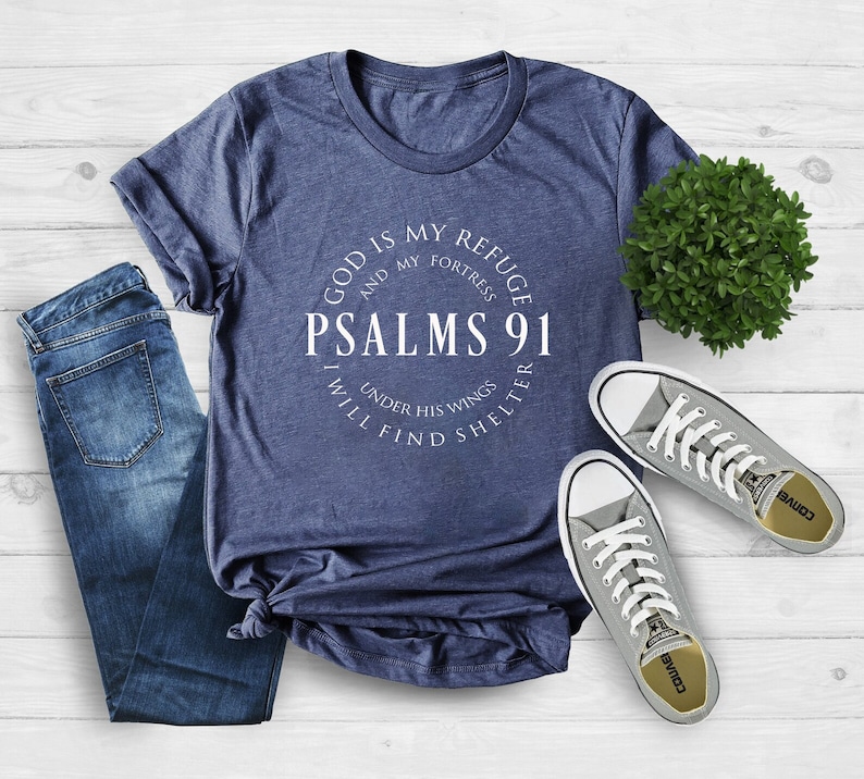 May include: A navy blue t-shirt with a white circle graphic that says "God is my refuge and my fortress Psalms 91 I will find shelter under his wings".