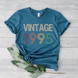 May include: A teal blue t-shirt with the text "Vintage 1995" in a retro font with colorful accents.