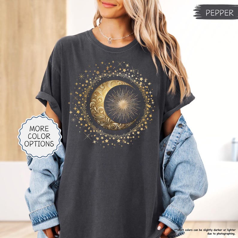 May include: Dark gray t-shirt featuring a gold crescent moon and sun design surrounded by gold stars. The shirt has rolled-up sleeves and the text "MORE COLOR OPTIONS" is visible. The word "PEPPER" is also visible.