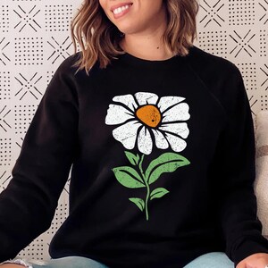 May include: Black sweatshirt with a white daisy graphic. The daisy has a yellow center and green leaves.