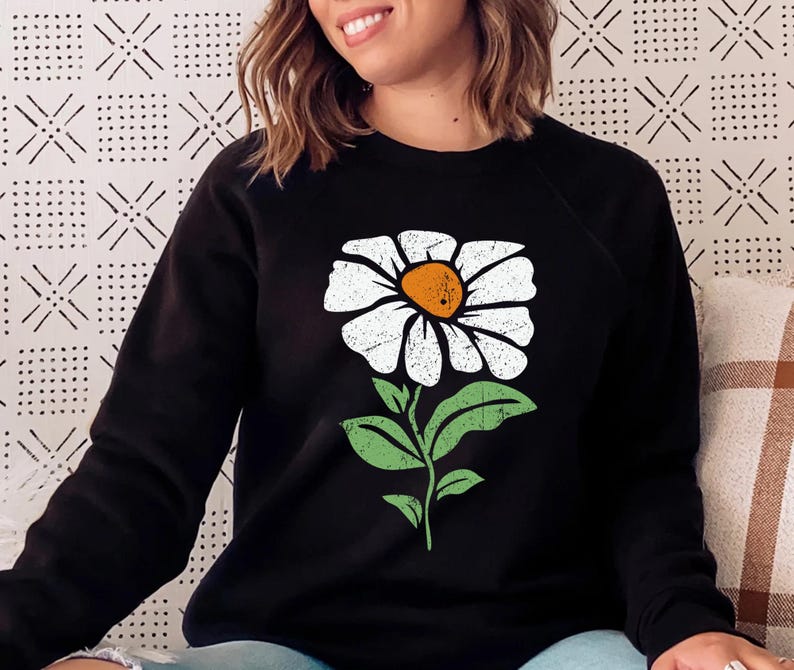 May include: Black sweatshirt with a white daisy graphic. The daisy has a yellow center and green leaves.