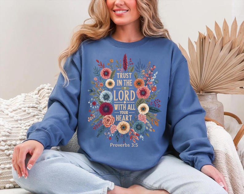 Peut inclure: Un sweat-shirt bleu avec un motif floral et le texte "Trust in the Lord with all your heart" et "Proverbes 3:5". Le motif floral comprend des fleurs dans les tons de rouge, rose, jaune et bleu.