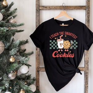 May include: Black t-shirt with a white and red graphic of a glass of milk and a cookie with the text "I teach the smartest cookies".
