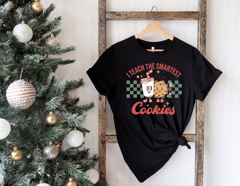 May include: Black t-shirt with a white and red graphic of a glass of milk and a cookie with the text "I teach the smartest cookies".