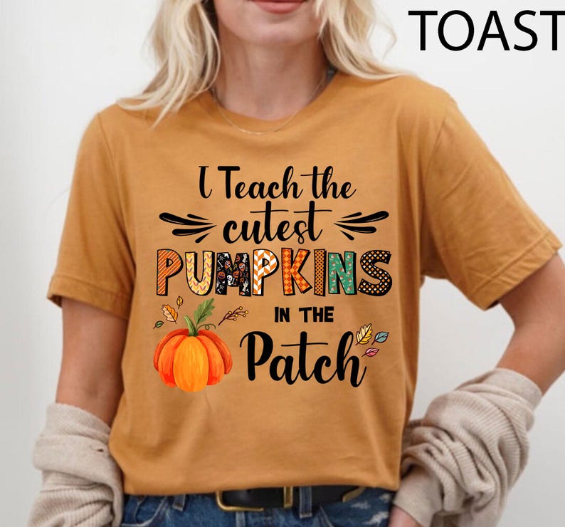 May include: Mustard-coloured t-shirt with the text "I Teach the Cutest Pumpkins in the Patch." The design includes a colourful pumpkin graphic and autumn leaves. The shirt is a comfortable, casual style.