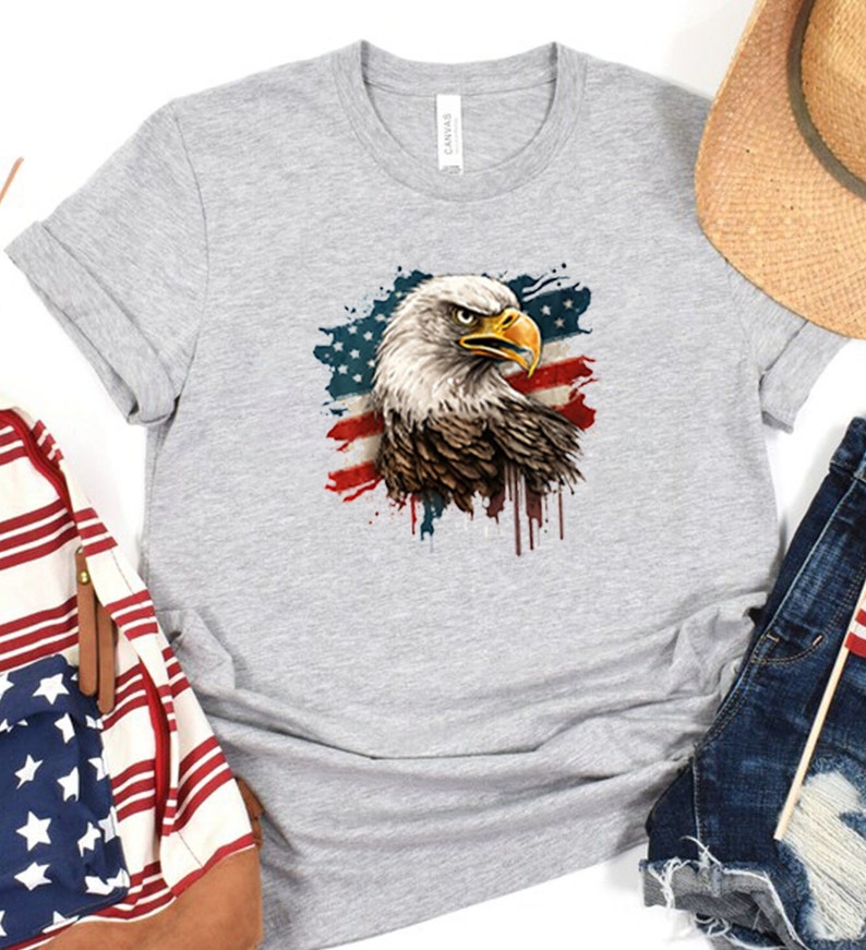May include: A gray t-shirt with a graphic of a bald eagle in front of an American flag with paint splatters. The eagle's head is turned to the right and its beak is open.