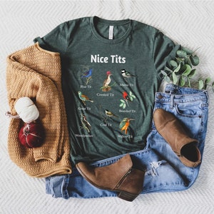 May include: A green t-shirt with the text "Nice Tits" and illustrations of different types of birds with their names below each bird. The birds include a blue tit, crested tit, great tit, willow tit, coal tit, bearded tit, woodpecker, and matsu tit.