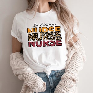 May include: White t-shirt with the text "future nurse" in a leopard print design with orange, yellow, and red accents.