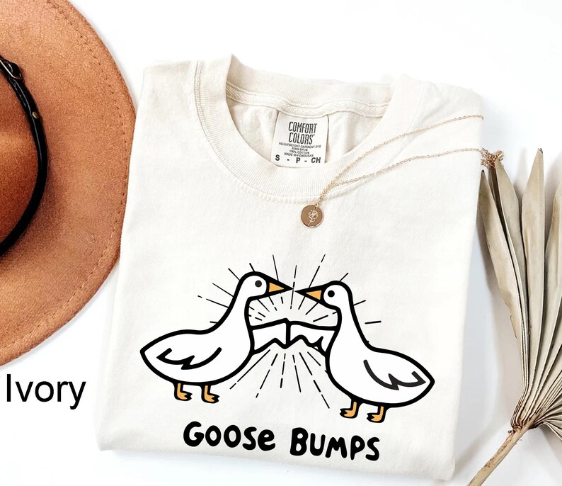 May include: Ivory t-shirt featuring a graphic of two geese facing each other with the text "Goose Bumps" below.