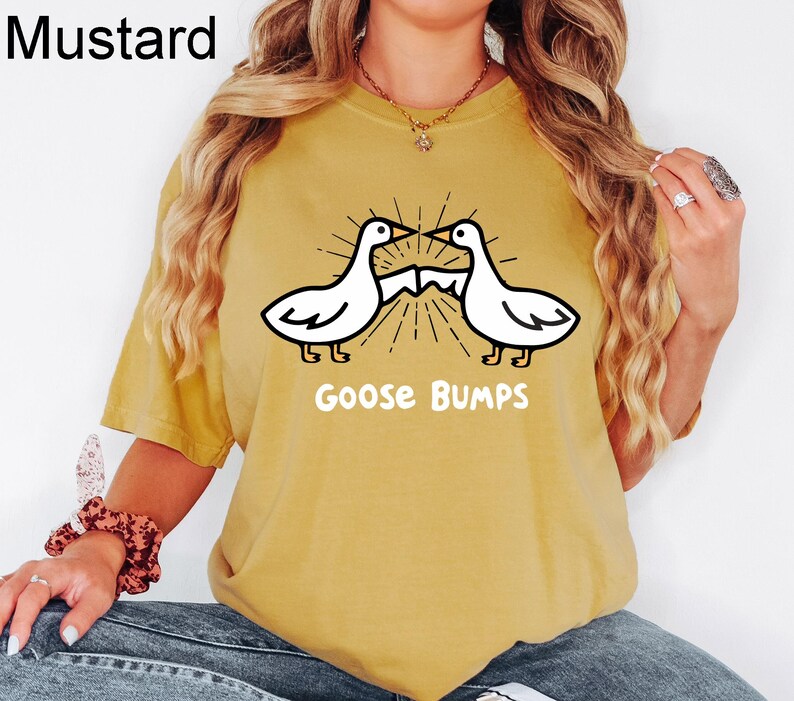 May include: A mustard yellow t-shirt featuring a graphic of two geese facing each other with the text "Goose Bumps" underneath.