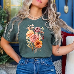 May include: A green t-shirt with a floral print featuring orange, pink, and red flowers. The flowers are surrounded by green leaves and stems.