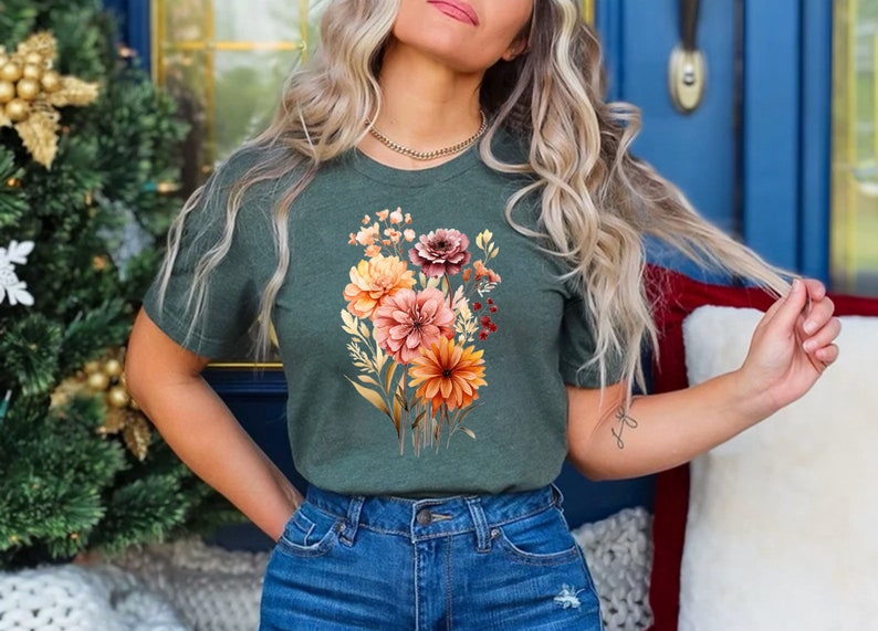 May include: A green t-shirt with a floral print featuring orange, pink, and red flowers. The flowers are surrounded by green leaves and stems.