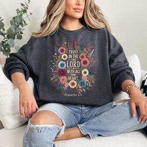 Peut inclure: Sweat-shirt gris fonc&eacute; avec un motif floral et le texte "Trust in the Lord with all your heart" et "Proverbes 3:5". Le motif floral comprend des fleurs roses, bleues et jaunes.