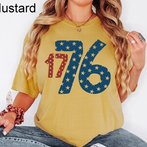 Puede incluir: Una camiseta amarilla mostaza con un gr&aacute;fico rojo y azul del n&uacute;mero 176 con estrellas. El gr&aacute;fico est&aacute; formado por estrellas rojas y azules sobre un fondo blanco.