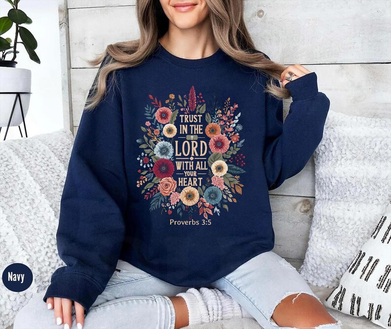 Peut inclure: Sweat-shirt bleu marine avec un motif floral et le texte "Trust in the Lord with all your heart" et le verset biblique Proverbes 3:5. Le motif comprend des fleurs et des feuilles color&eacute;es.