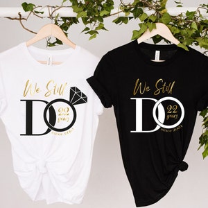 May include: Two white and black t-shirts with the text "We Still Do" and a gold ring with the number 22 and the text "years since 2001".