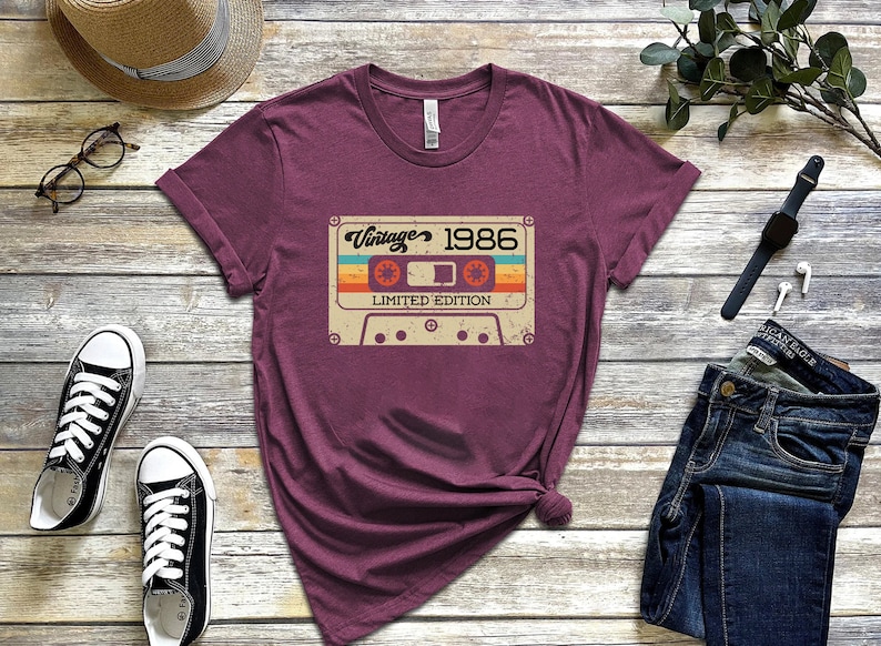 May include: A maroon t-shirt featuring a vintage cassette tape graphic that reads "Vintage 1986 Limited Edition".