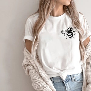 May include: A white t-shirt with a black bee graphic on the front. The bee is stylized and has wings spread out.