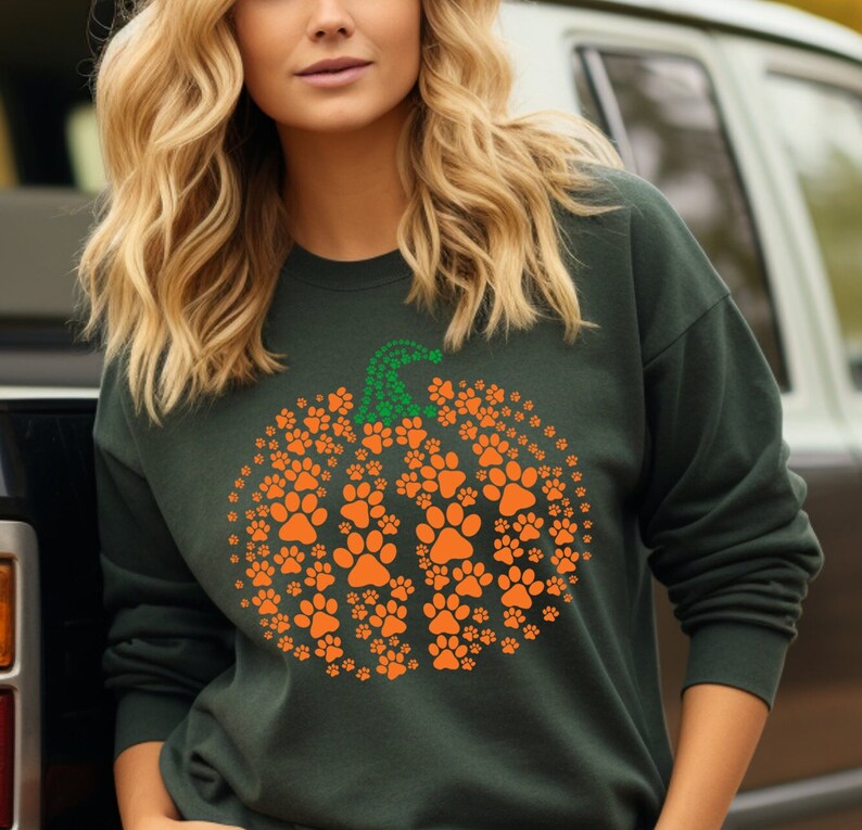 Peut inclure: Sweat-shirt vert fonc&eacute; avec un motif de citrouille compos&eacute; d'empreintes de pattes orange. La tige de la citrouille est faite d'empreintes de pattes vertes. Un design amusant et festif pour les amoureux des animaux, parfait pour l'automne.