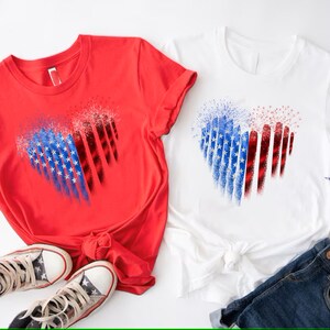 Pu&ograve; includere: Due magliette, una rossa e una bianca, ciascuna con un disegno a cuore. Il cuore &egrave; diviso in due met&agrave;, una con stelle blu e l'altra con strisce rosse, che ricordano la bandiera americana. Sono visibili anche un paio di scarpe da ginnastica a stelle e jeans.