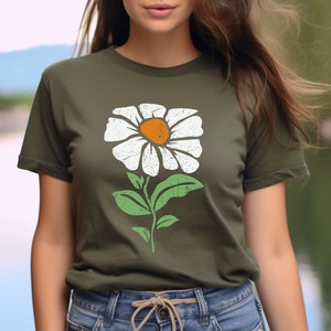 May include: A woman is wearing a green t-shirt with a white daisy flower graphic. The flower has a yellow center and green leaves.