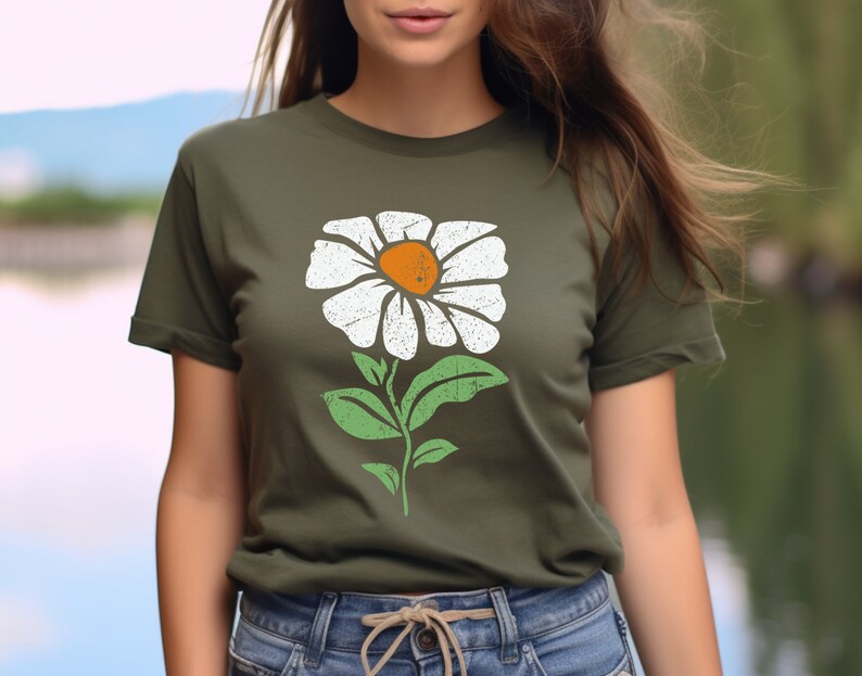 May include: A woman is wearing a green t-shirt with a white daisy flower graphic. The flower has a yellow center and green leaves.