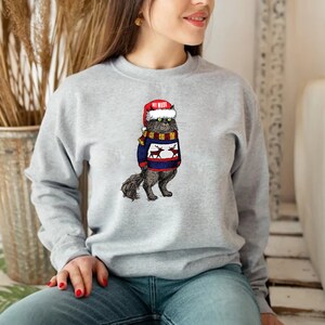 K&ouml;nnte beinhalten: Ein graues Sweatshirt mit einem Aufdruck eines Katers, der einen Weihnachtsmann-Hut und einen Weihnachtspullover mit Rentieren tr&auml;gt. Der Text auf dem Hut lautet "My Mama".