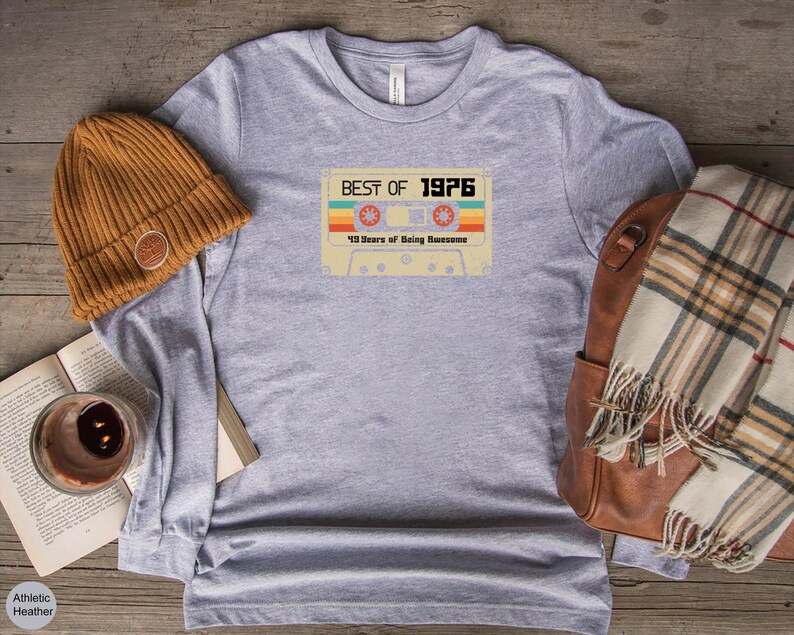 May include: A heather grey long-sleeved t-shirt with a vintage cassette tape design. The tape has the text "Best of 1976" and "49 Years of Being Awesome".